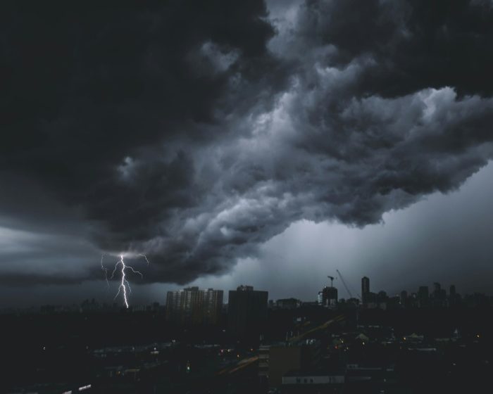 A dramatic storm looms over a city skyline, highlighted by a striking lightning bolt illuminating the dark clouds.