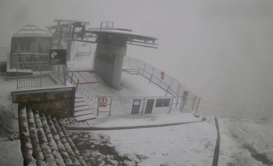 Snow-covered place and surrounding area in heavy fog, with fresh snowfall visible on the ground and railings.