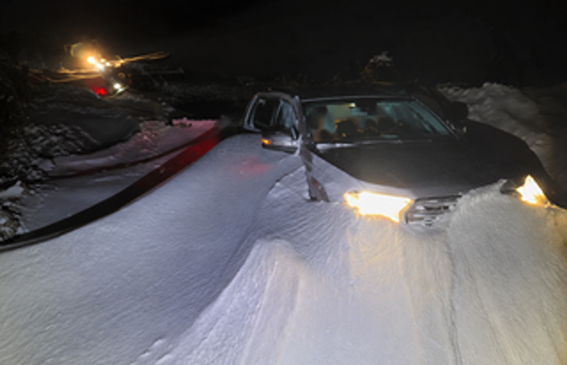 Car partially buried in deep snow during a severe winter storm in the Andes as rescue equipment operates nearby.